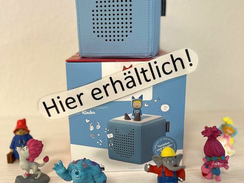 Das Bild zeigt eine hellblaue Tonie-Box mit dem Schild "Hier erhältlich!" und verschiedenen Tonie-Figuren in der Mittelpunktbibliothek Ehm Welk