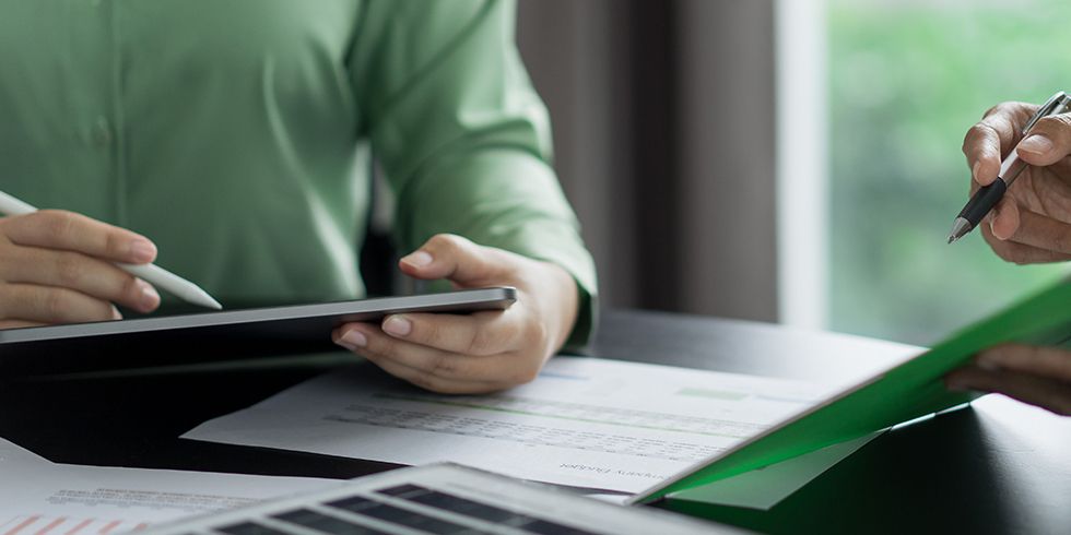 Nahaufnahme zwei Personen am Tisch, sitzend. Eine hält ein Tablet die Andere ein Klemmbrett mit Kugelschreiber. Vor ihnen liegt eine kleines Solarmodul.