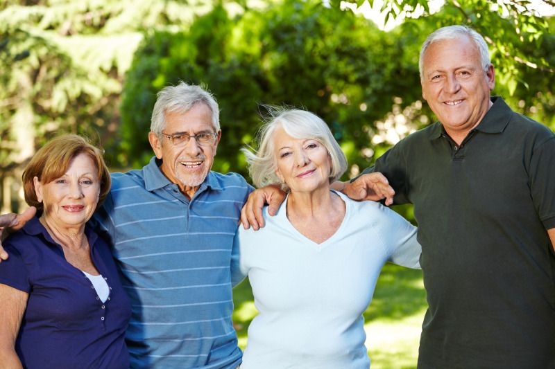 Zwei Seniorinnen und zwei Senioren stehen nah beieinander in einem Park und lächeln in die Kamera