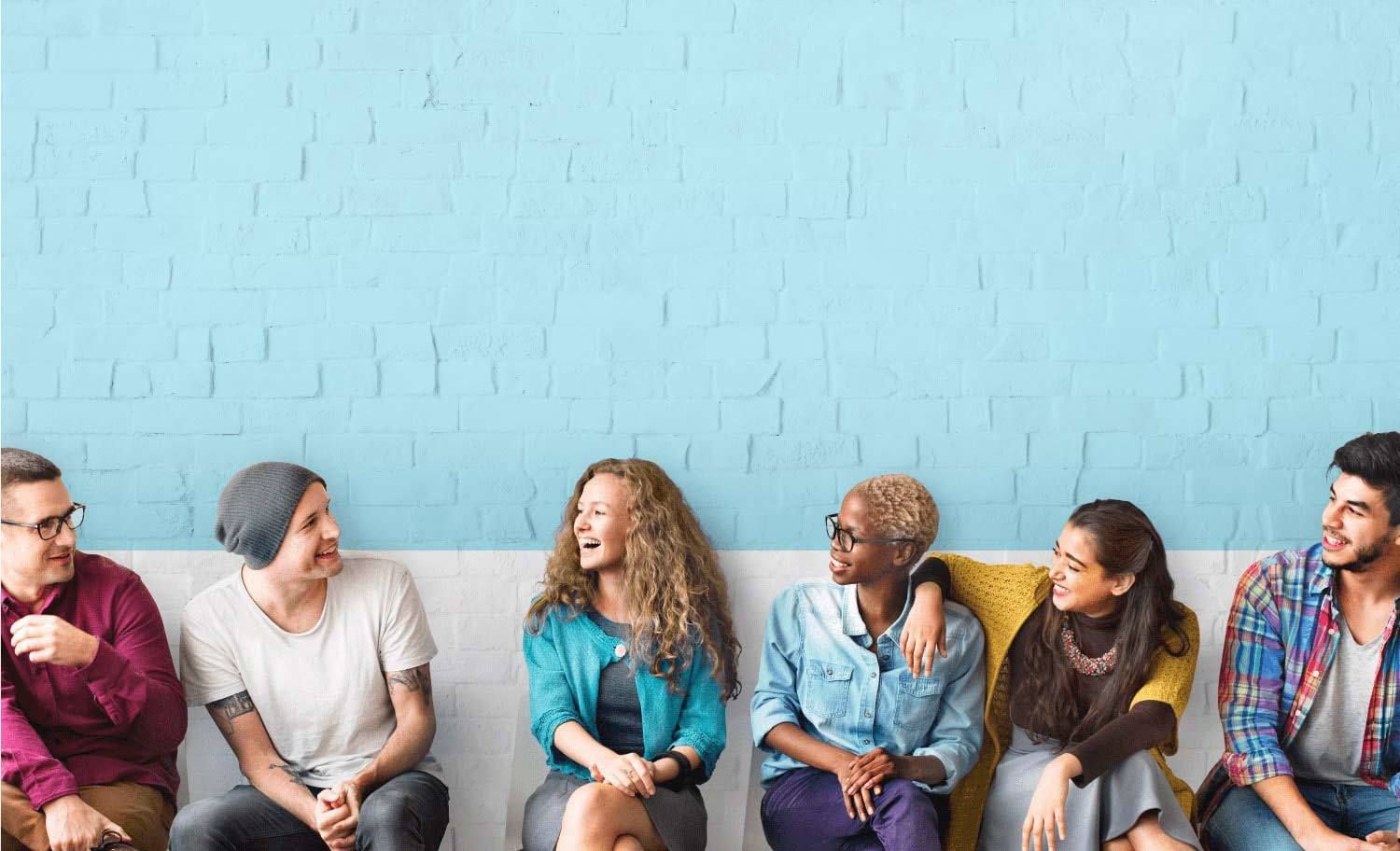 Eine Gruppe junger Menschen, die sich lachend ansehen, sitzt auf einem Sofa