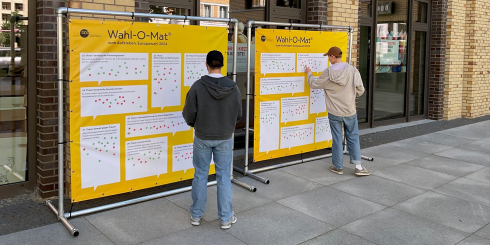 Der Wahl-O-Mat zum Aufkleben vor dem Besuchszentrum Ostkreuz: zwei Menschen kleben Punkte auf Stellwände