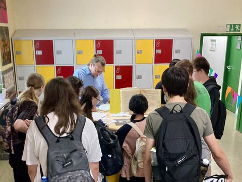 Bildvergrößerung: Kinder schauen zu einem Tisch, auf dem ein Ordner und unterschiedliche Dokumente ausgebreitet.