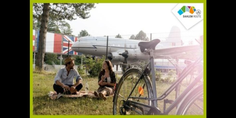 Foto zum Bewerben der Dahlem Route. Zwei Personen sitzen vor dem Alliierten Museum