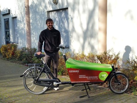 Bildvergrößerung: Kiezklub-Leiter des "Gerard Philipe" steht am neuen Lastenrad und freut sich über die Ausleihmöglichkeit