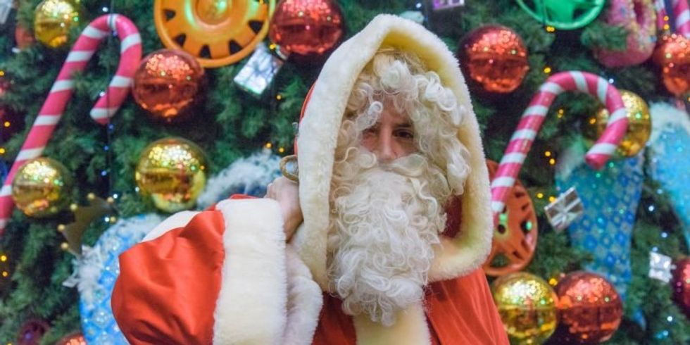 Weihnachtsmann mit großem Geschenkesack vor einem geschmückten Weihnachtsbaum