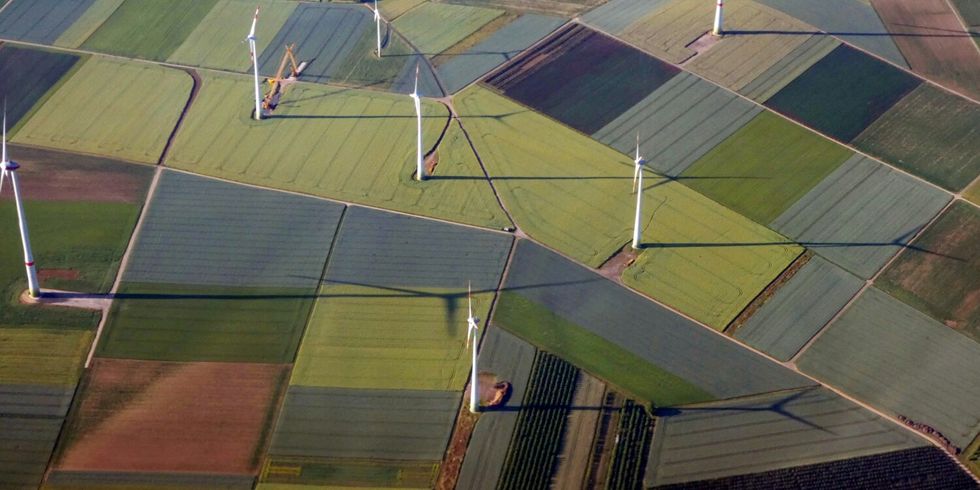 Vogelperspektive auf verschiedenfarbige landwirtschaftliche Felder mit vereinzelten Windrädern