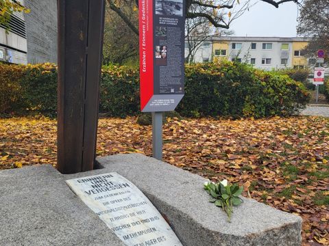 Bildvergrößerung: Hinter einem Gedenkstein mit einer darauf abgelegten Rose steht eine weitere Gedenktafel.