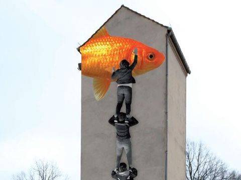 Bildvergrößerung: Auf einem Turm ist ein großes Bild zu sehen. Das Bild zeigt mehrere Jungs in schwarz-weiß. Der oberste junge streckt sich zu einem großen orangenen Goldfisch.