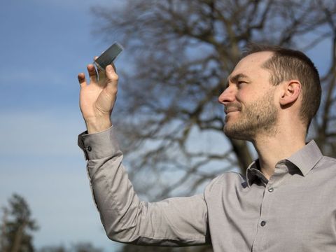  Mann hält kleine semitransparente Solarzelle in Richtung des Himmels 
