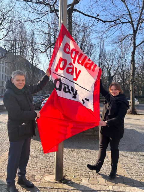 Ein Mann und eine Frau halten eine Equal Pay Day Fahne