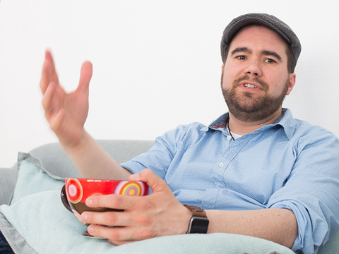 Benajmin Floer sitzend mit einer bunten Kaffeetasse in der Hand