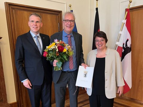 Martin Jammer hält Urkunde. Neben ihm stehen der Chef der Senatskanzlei und die Präsidentin des Rechnungshofs