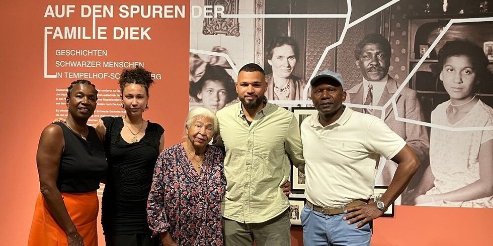 Fünf Familienmitglieder aus drei Generationen stehen vor der Eröffnungswand der Ausstellung über die Familie Diek im Schöneberg Museum. Abenaa (links) und Roy Adomako (rechts) mit Familienmitgliedern in der Ausstellung