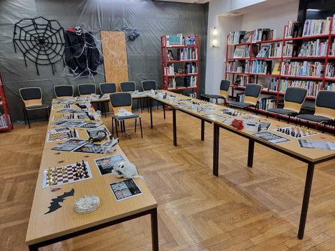 Das Foto zeigt mehrere Tische mit Schachbrettern darauf. Im Hintergrund sind Halloween-Schmuckelemente zu sehen.