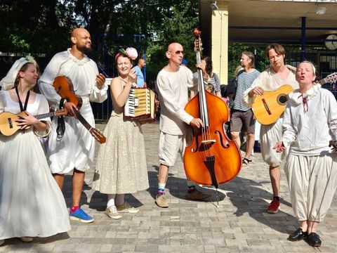 Bildvergrößerung: Auf einem Platz stehen mehrere Personen mit Musikinstrumenten nebeneinander und musizieren.