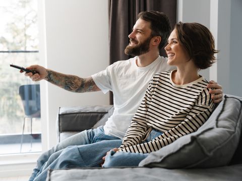 glückliches weißes Paar schaut TV und sitzt auf einer Couch