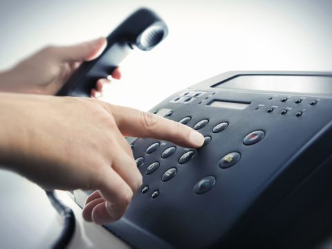 Eine Hand wählt eine Rufnummer auf dem Telefon