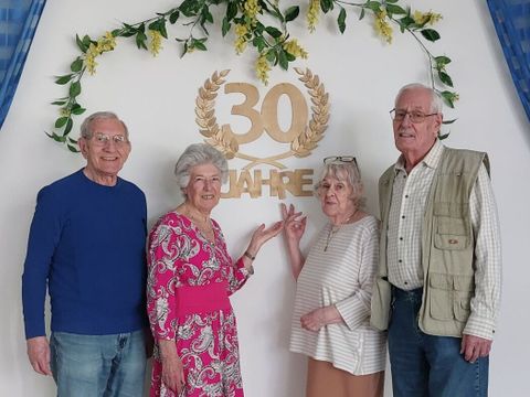 Bildvergrößerung: Vier ältere Personen stehen neben einer Wand, an der 30 Jahre steht.