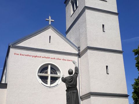 Bildvergrößerung: Auf einer Kirche ist das schwarz-weiß Bild von einem Redemptoristen, der auf die Fassade in rot den Spruch "Die Barmherzigkeit erhebt sich über das Gericht" schreibt.