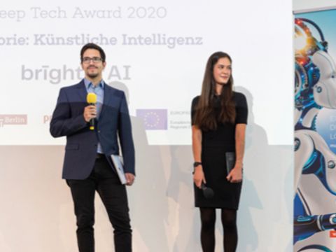 Ein Mann hält ein Mikrofon, daneben steht eine Frau mit einem Award in der Hand