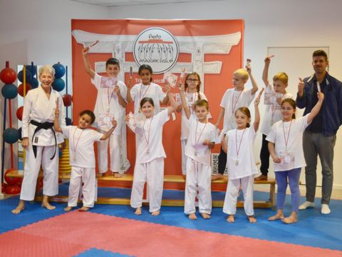 Bildvergrößerung: Kinder posieren in einer Judohalle mit Medaillen, Urkunden und Süßigkeiten.