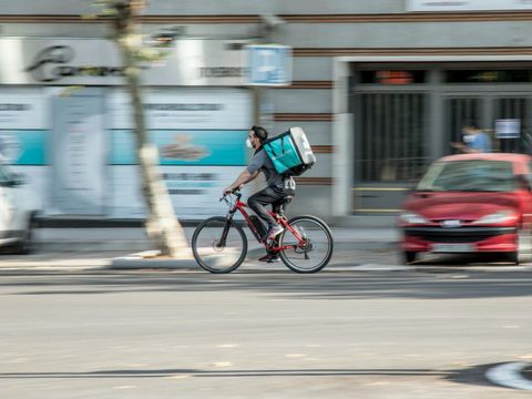 Ein Mitarbeiter eines Lieferdienstes fährt mit dem Fahrrad auf der Straße. 