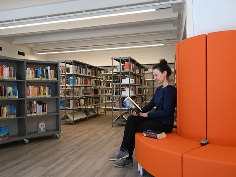 Das Foto zeigt die Leiterin der Bibliothek Maria Galey in der Bibliothek auf einem roten Sofa sitzend.