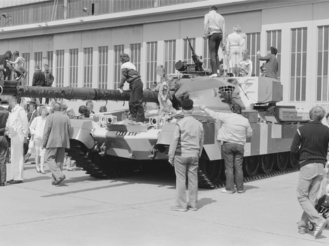 Bildvergrößerung: Eine schwarz-weiß Fotografie von einem Panzer. Um den Panzer herum und auch auf dem Panzer stehen Menschen.