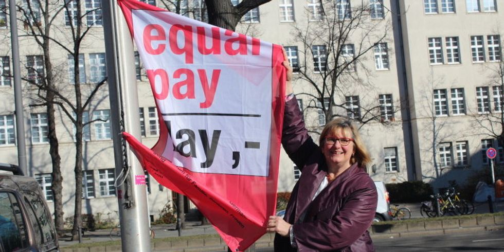 Eine Frau hält eine Fahne an einem Mast mit der Aufschrift Equal Pay Day