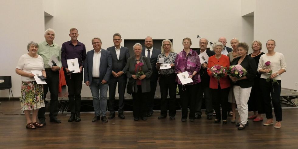 Eine Gruppe Menschen steht auf einer Bühne und lächelt in die Kamera. Viele halten einen Strauß oder eine Mappe mit dem Berliner Wappen.