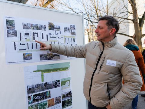 Ein Gebietsbeauftragter zeigt auf Stelltafel mit Plänen und Fotos