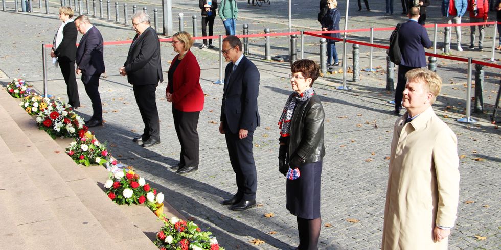 Sieben Personen stehen vor Treppenstufen mit Blumengestecken