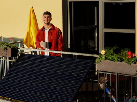 Lächelnder Mann auf Balkon in der Sonne. Am Balkon ist ein Solarmodul angebracht.
