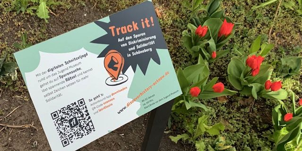 Eine Tafel mit dem Track it Logo und QR- Code steht neben Tulpen.