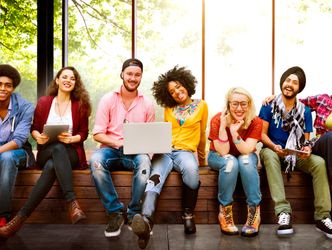 Junge Menschen diverse Herkunft sitzen lächelnd auf einer Bank