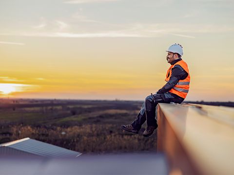 Mann in Arbeitskleidung auf Dach schaut in die Ferne