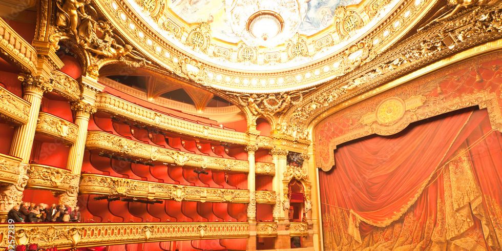 Innenaufnahme eines Theaters mit vier Rängen, roten Sitzen und Bühnenvorhang