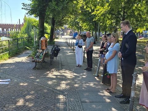 Bezirksstadtrat Max Kindler und der Vorsteher der Bezirksverordnetenversammlung Werner Heck und mehrere Anwesende beim stillen Gedenken am May-Ayim-Ufer in Kreuzberg