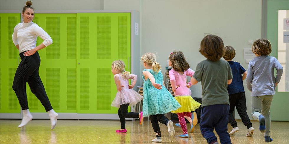 Tanzend bewegen im Kreis. Carina Otte und eine Gruppe von Kindern - von hinten betrachtet.