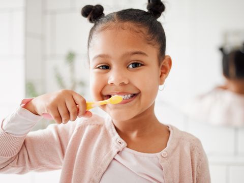 One mixed race adorable little girl brushing her teeth in a bathroom at home. A happy Hispanic child with healthy daily habits to prevent cavities and strengthen enamel