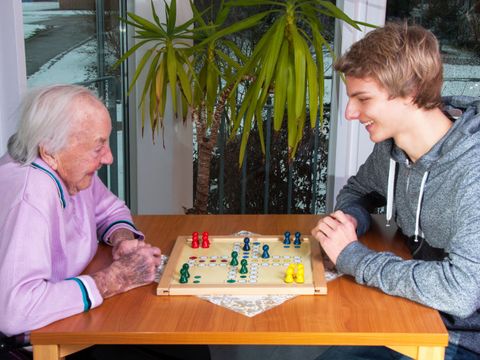 Ein Jugendlicher spielt mit einer Seniorin ein Brettspiel