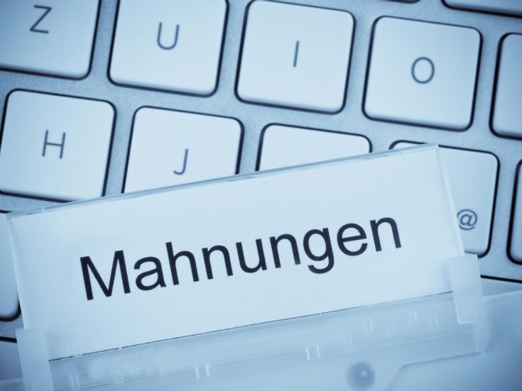 Auf einer Computertastatur liegt ein Hängeregister mit der Aufschrift 'Mahnungen'