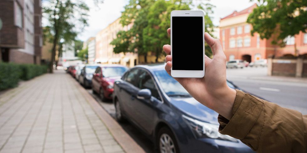 Mann hält Handy vor parkenden Autos hoch