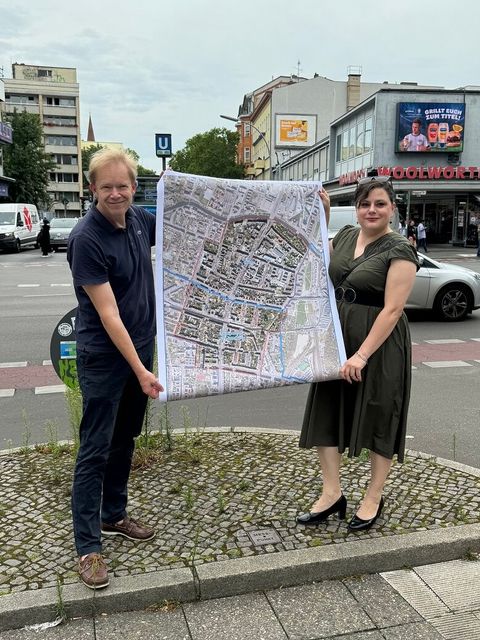 Bildvergrößerung: Eine Frau und ein Mann stehen an einer Straßenkreuzung und halten einen Stadtplan hoch