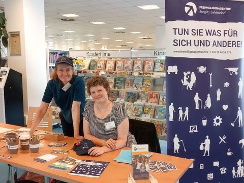 Bildvergrößerung: Zwei Menschen der Freiwilligenagentur Steglitz-Zehlendorf an einem Informationsstand in der Ingeborg-Drewitz-Bibliothek