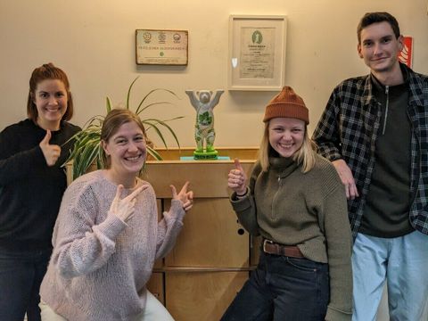 Bildvergrößerung: Vier Personen stehen neben einer Bärenfigur, einem Green Buddy Award. Sie zeigen auf die Figur oder zeigen den Daumen nach oben.