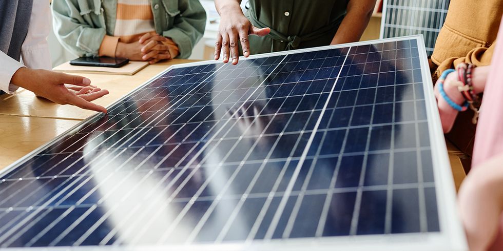 Solarmodul auf Tisch, mehrere Personen stehen drum herum, man sieht Hände die auf das Modul zeigen