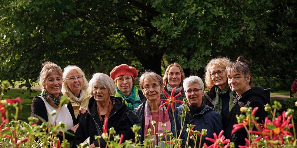 Die Teilnehmerinnen der Frauenkunstkarawane stehen gemeinsam hinter einem Beet mit blühenden Dahlien