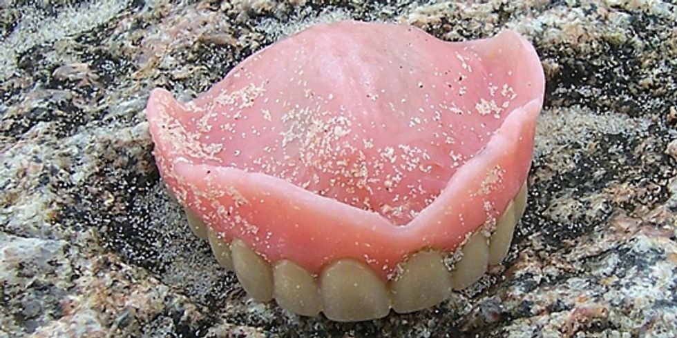 buehne_Zahnprotese mit Sand bestreut auf einem Stein liegend