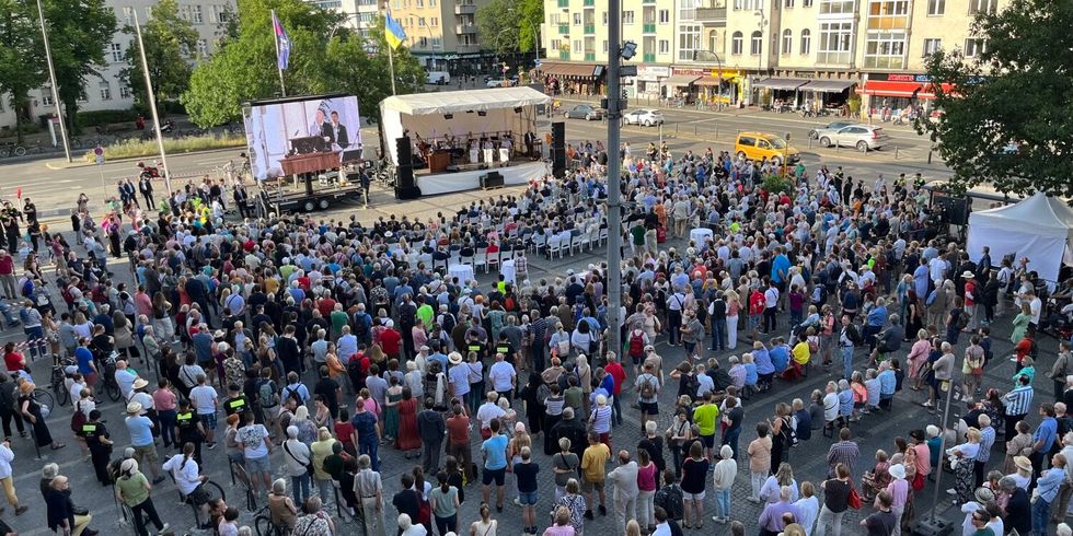 Die Draufsicht auf einen Platz mit einer großen Menge an Menschen. Sie schauen in die Richtung einer Bühne und einer Großbildleinwand.